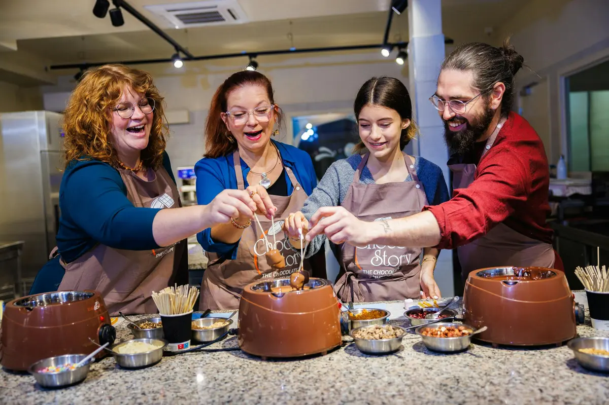 Trois personnes portant des tabliers préparent ensemble des friandises au chocolat sur une table avec des fontaines à chocolat et des garnitures.