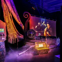 Un présentoir avec une proue de navire viking, un bouclier et un écran montrant des acteurs dans une scène dramatique, le tout entouré d'un éclairage tamisé. &copy; ®Cités Immersives