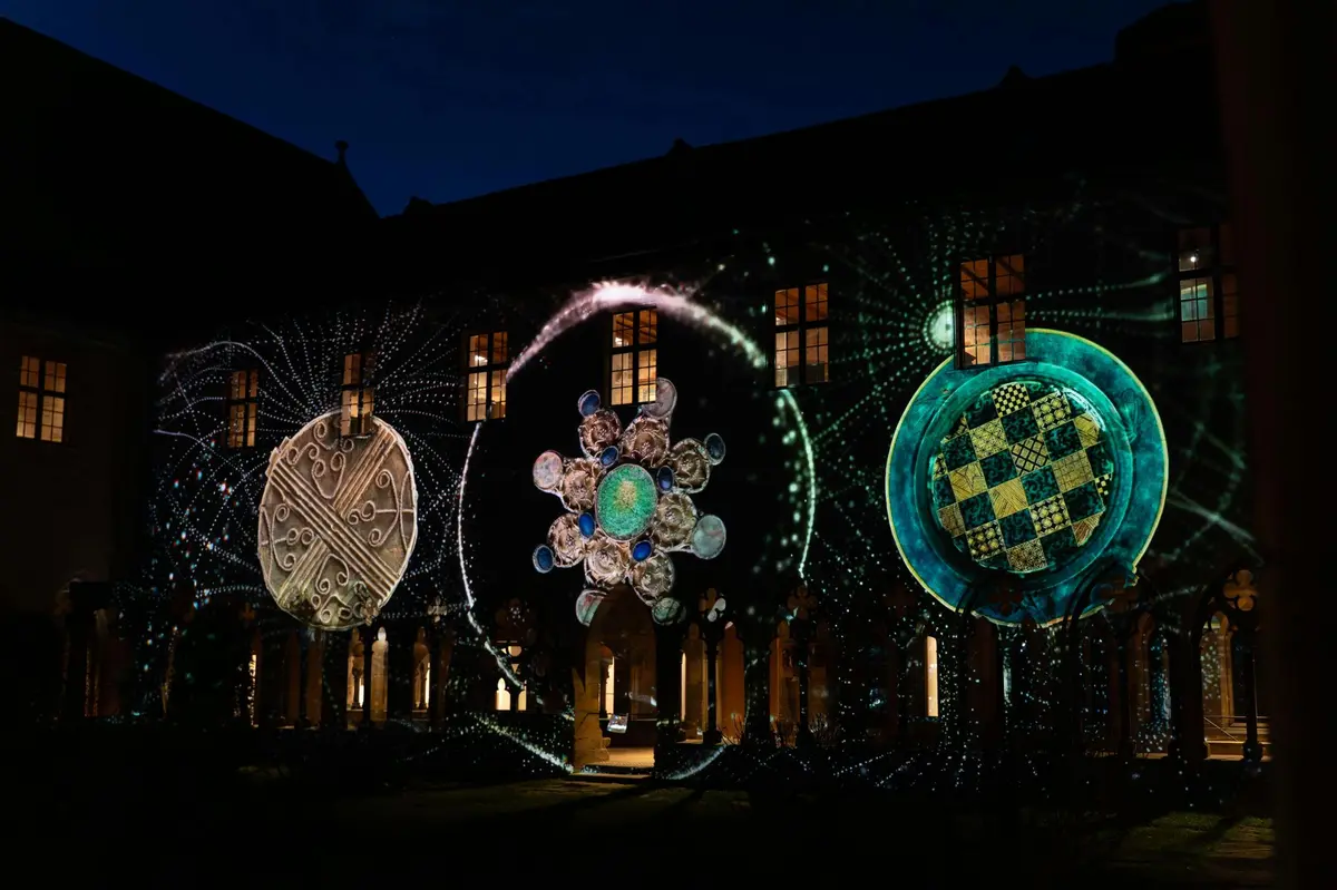Une scène nocturne montrant la façade illuminée d'un bâtiment, sur laquelle se dessinent des projections lumineuses circulaires très détaillées.