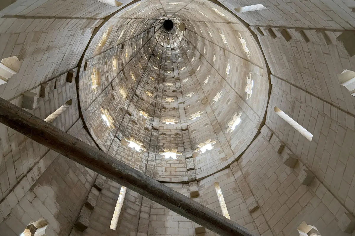Vue int&eacute;rieure d'un &eacute;difice haut et cylindrique en pierre, dot&eacute; de fen&ecirc;tres cintr&eacute;es et d'une poutre qui traverse l'image au premier plan.