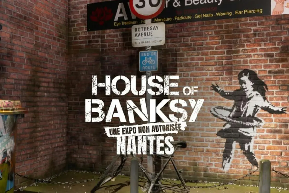 Un mur orné de graffitis et d'une pancarte sur laquelle on peut lire, en lettres blanches en gras : « House of Banksy, Une Expo Non Autorisée, Nantes ».