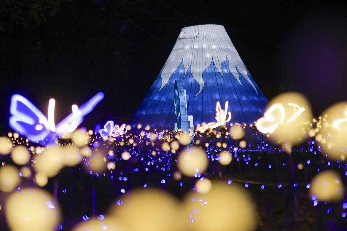 A bright blue and white illuminated tent-like structure surrounded by glowing blue and yellow lights at night.