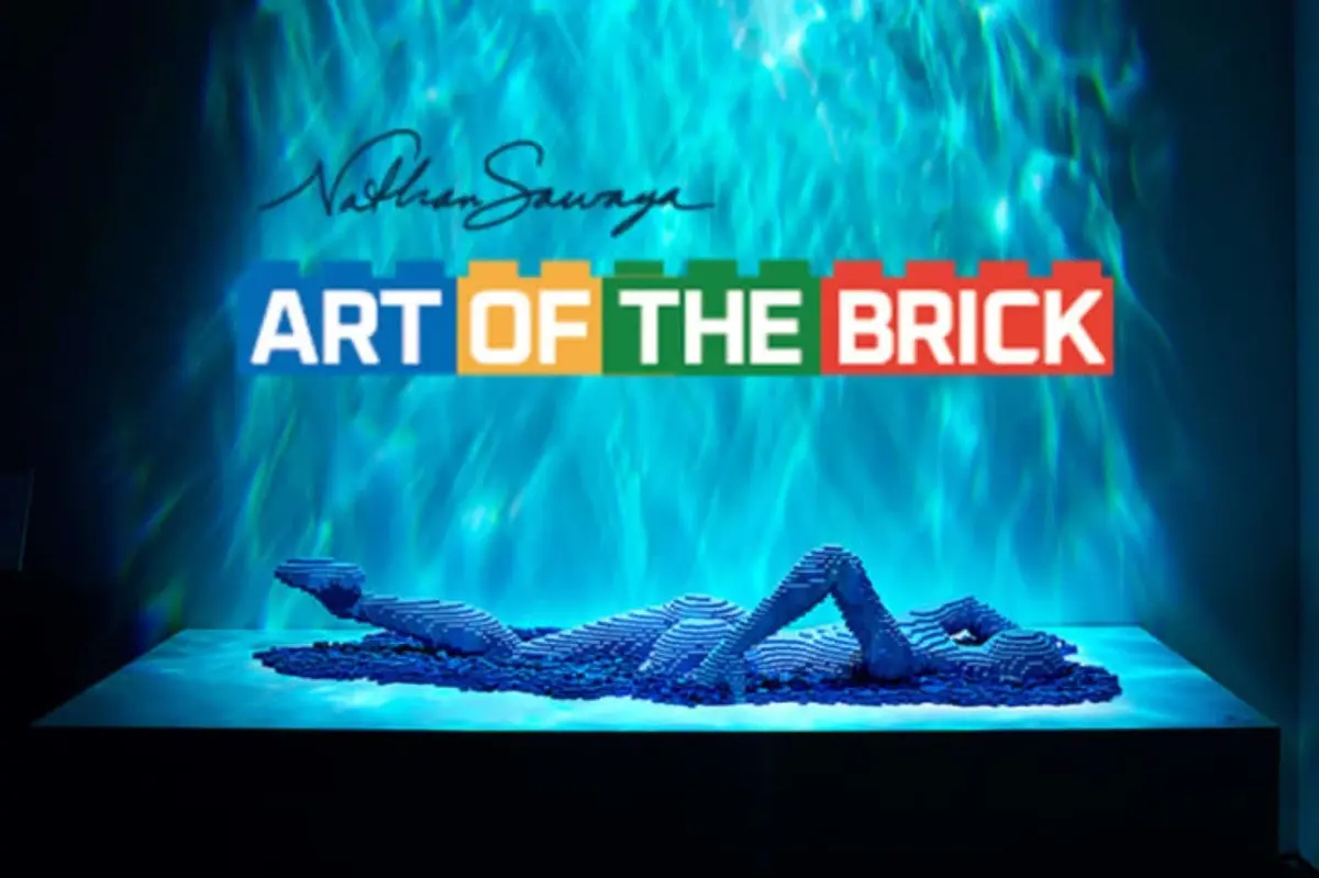 Une sculpture en Lego représentant un personnage allongé, sous l'inscription « Art of the Brick », sur un fond éclairé de bleu.