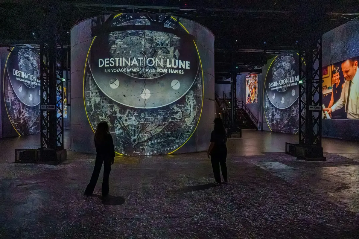 Deux personnes à l'intérieur d'une exposition immersive comprenant de grands écrans circulaires avec des images liées à la lune et le texte Destination Lune.