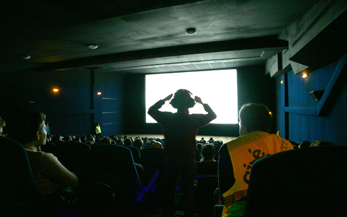 Un spectateur est debout, mains sur la tête avec un casque anti-bruit. Il profite de la séance avec et comme tout le monde.