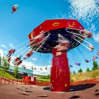 Un carrousel rouge en mouvement sur fond de ciel bleu avec des personnes assises et un ballon flottant à proximité. DR