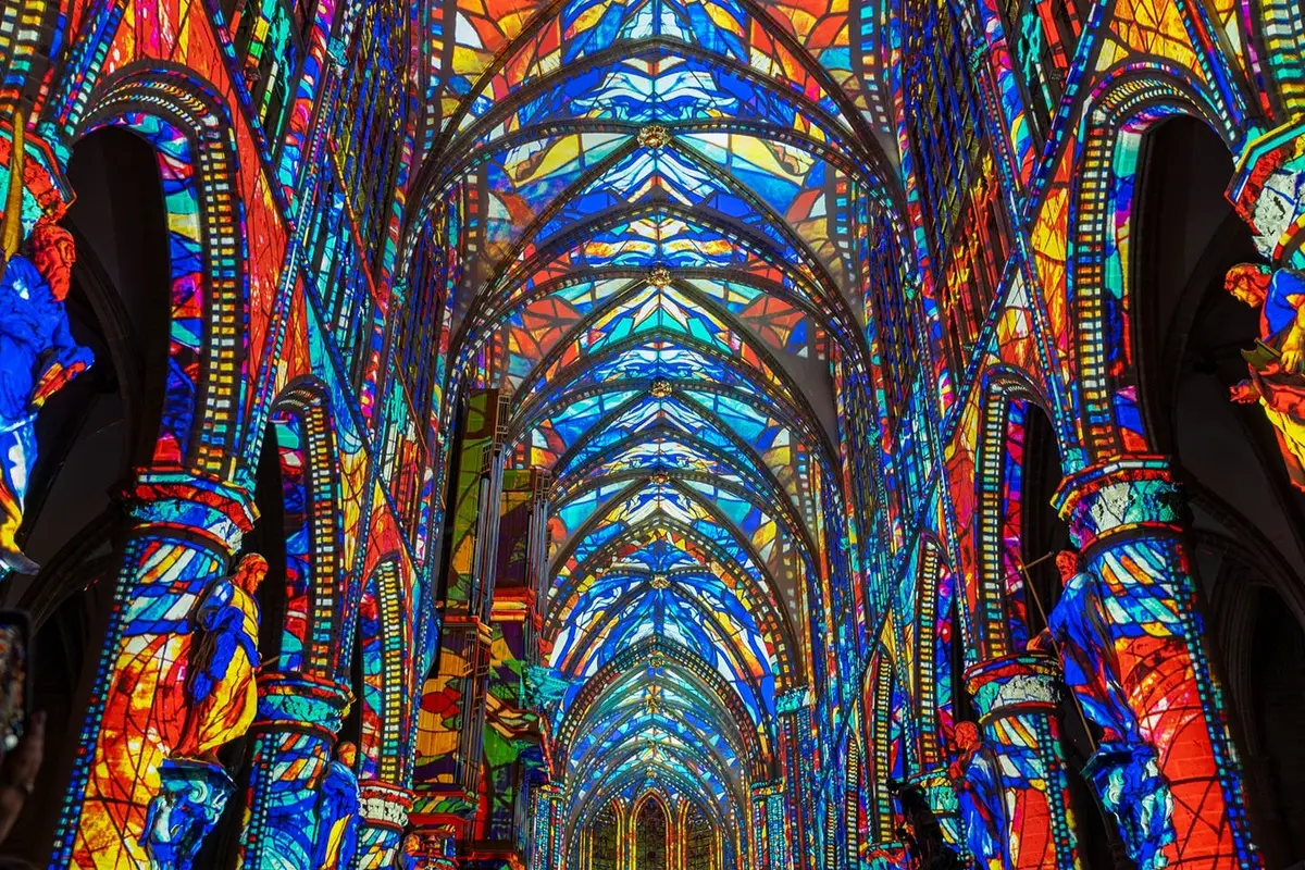Intérieur d'une cathédrale orné de vitraux colorés, avec des plafonds voûtés et des motifs complexes.