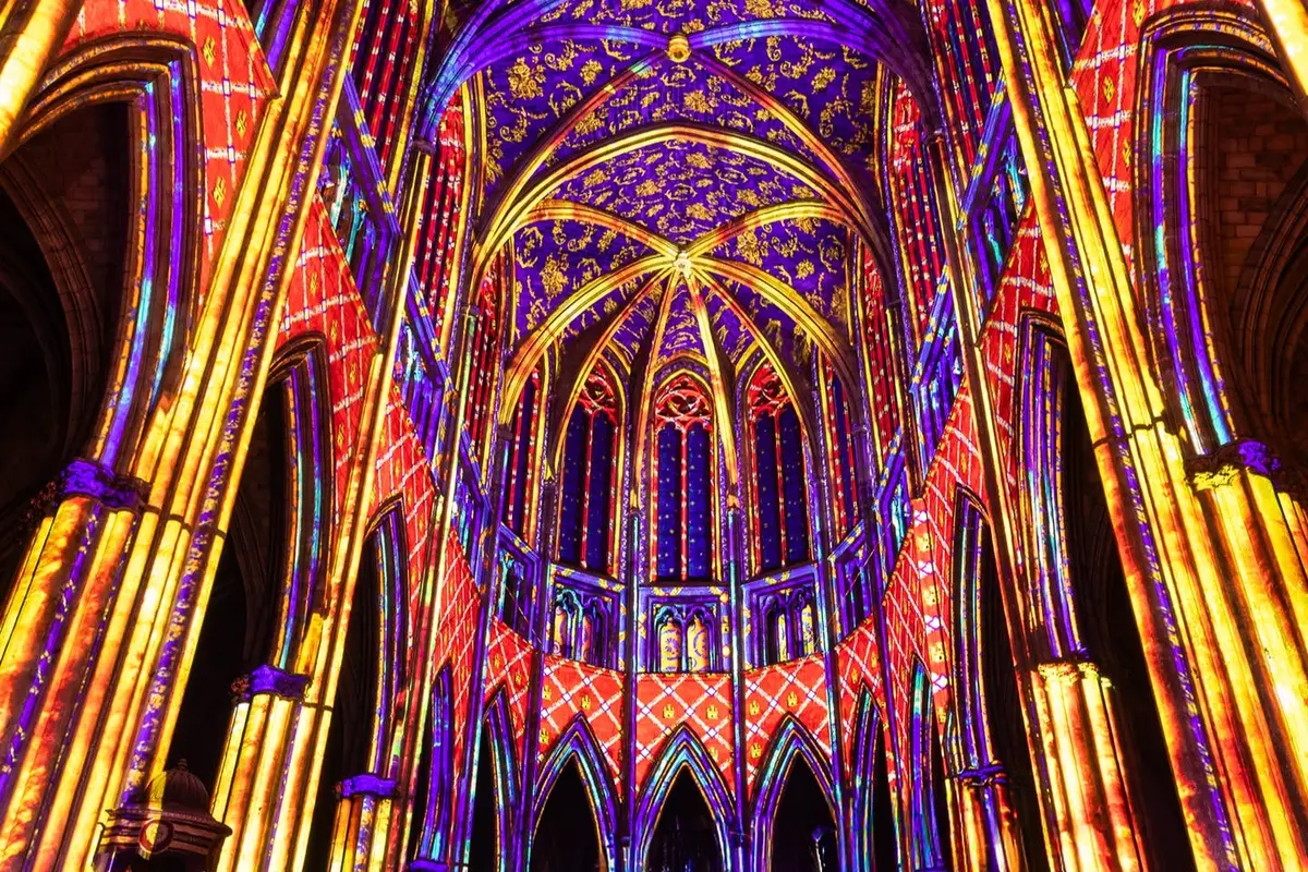 Intérieur d'une cathédrale gothique éclairé par des lumières colorées, mettant en valeur les arcs, les motifs et la voûte.
