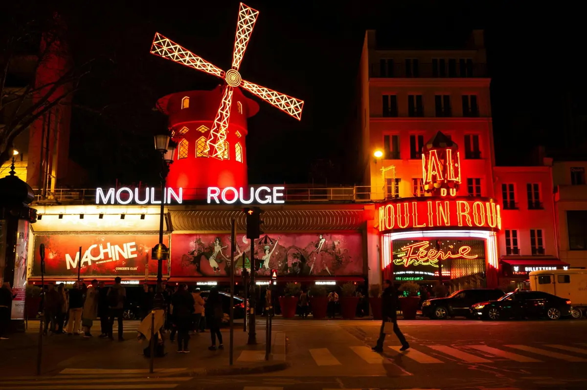 La façade illuminée du Moulin Rouge la nuit, avec son moulin rouge emblématique et ses enseignes au néon.