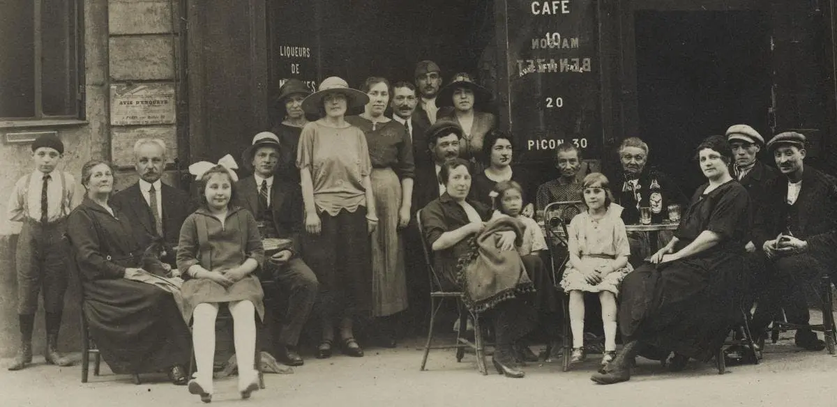 Un groupe d'hommes, de femmes et un enfant posent à l'extérieur d'un bâtiment avec des panneaux sur le mur. Une femme et un homme sont assis.