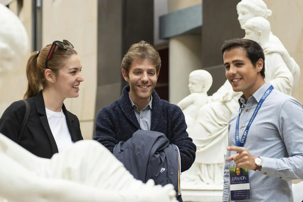 Trois personnes discutent et sourient à l'intérieur d'un musée, entourées de statues de marbre blanc.