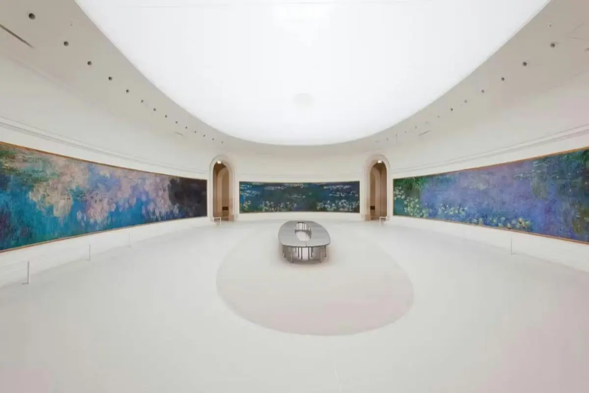 Une vaste salle d'exposition aux murs incurvés, où sont exposés de grands tableaux impressionnistes, avec au centre un banc ovale.