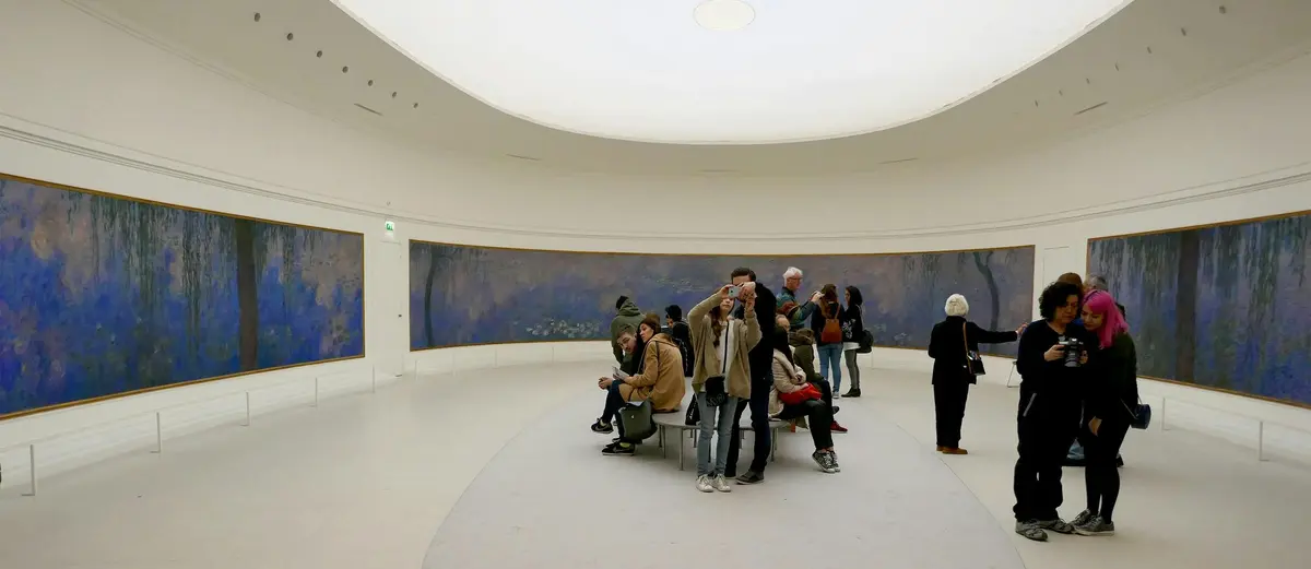 Des personnes observent une grande peinture panoramique dans une galerie de musée avec un plafond blanc incurvé et des bancs au centre.