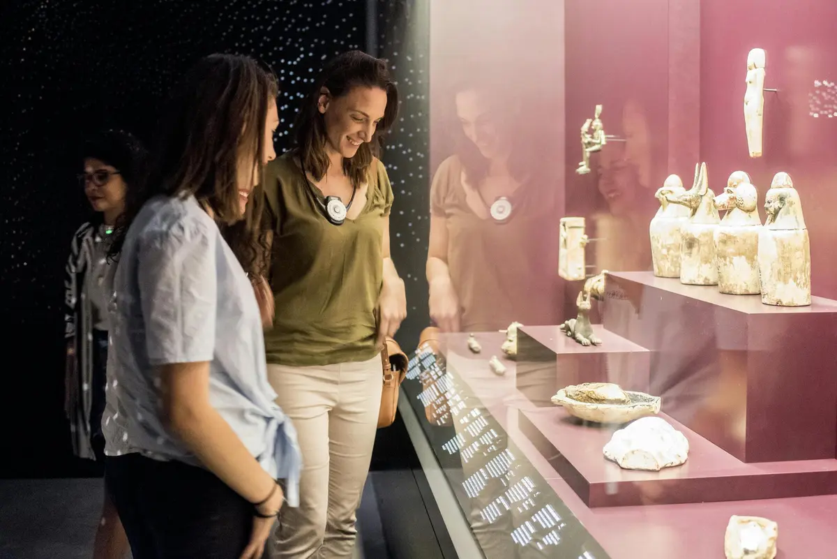 Trois femmes regardent des objets présentés dans une vitrine lors d'une exposition dans un musée.