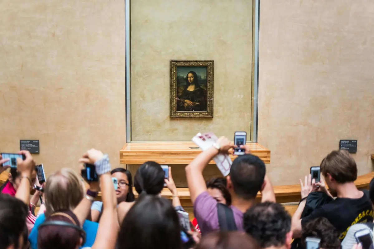 Groupe de touristes prenant des photos de Mona Lisa à l'intérieur du musée du Louvre.