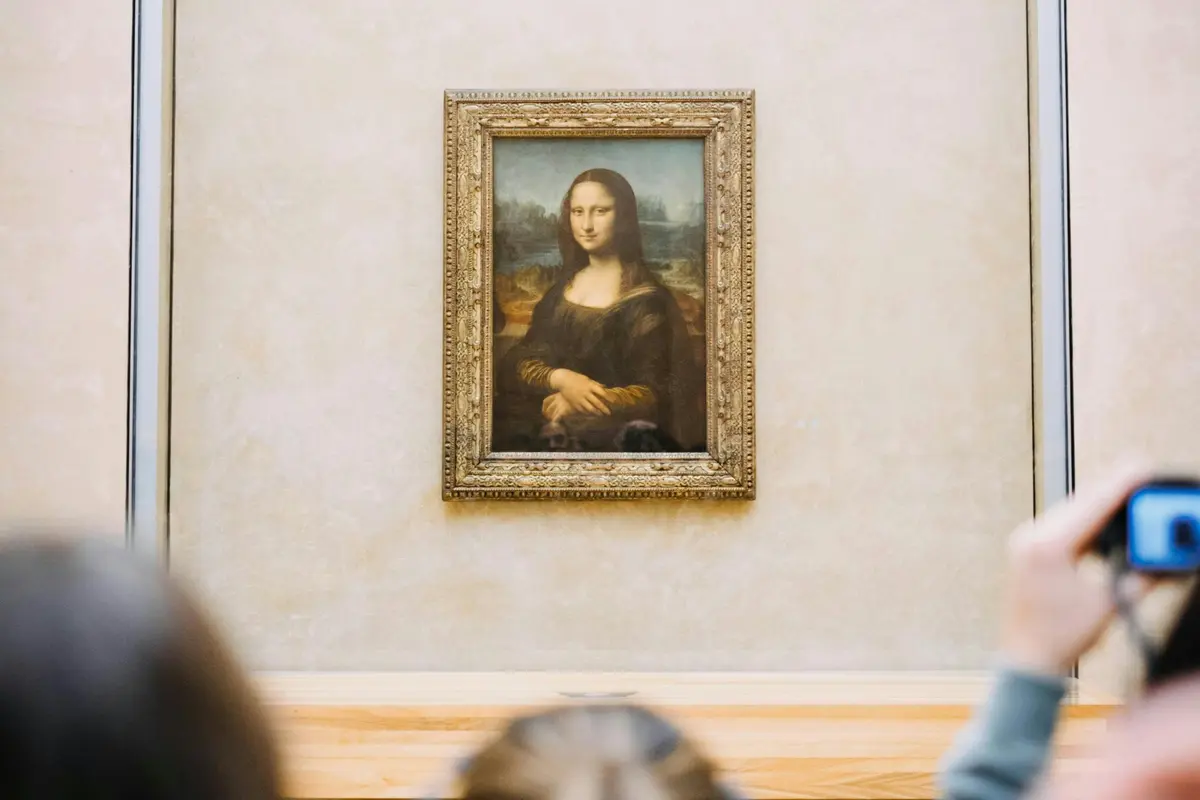 Un portrait encadré de la Joconde affiché sur un mur avec des têtes floues de spectateurs au premier plan.
