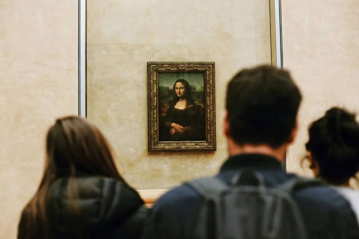 Deux personnes, le dos tourné, regardent la Joconde encadrée sur un mur beige dans un musée.