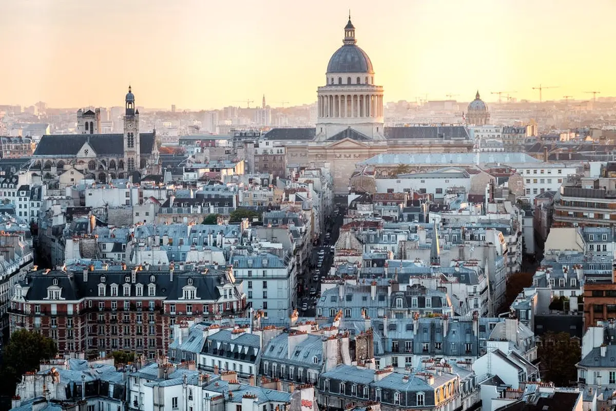 Vue de la ville de Paris au coucher du soleil, avec le dôme du Panthéon en évidence parmi les toits et les bâtiments.