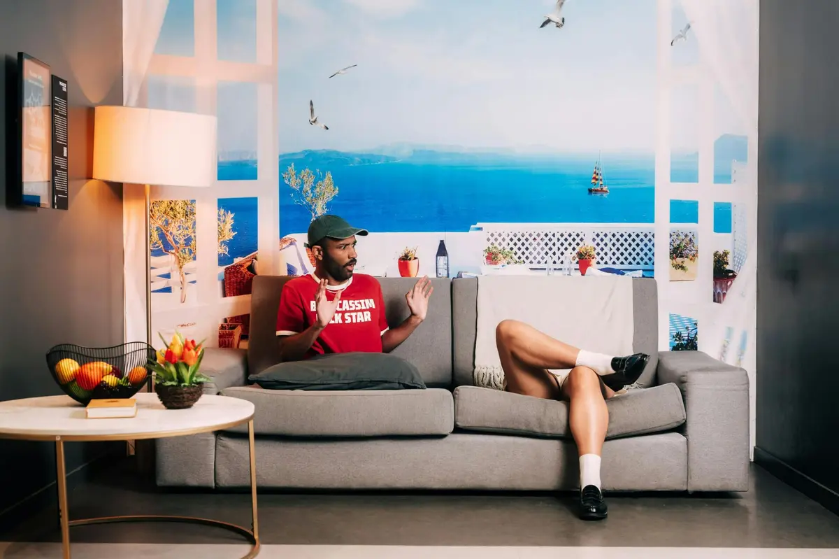 Deux personnes assises sur un canapé gris dans une pièce au décor côtier, une table d'appoint avec des fleurs et des fruits à proximité.