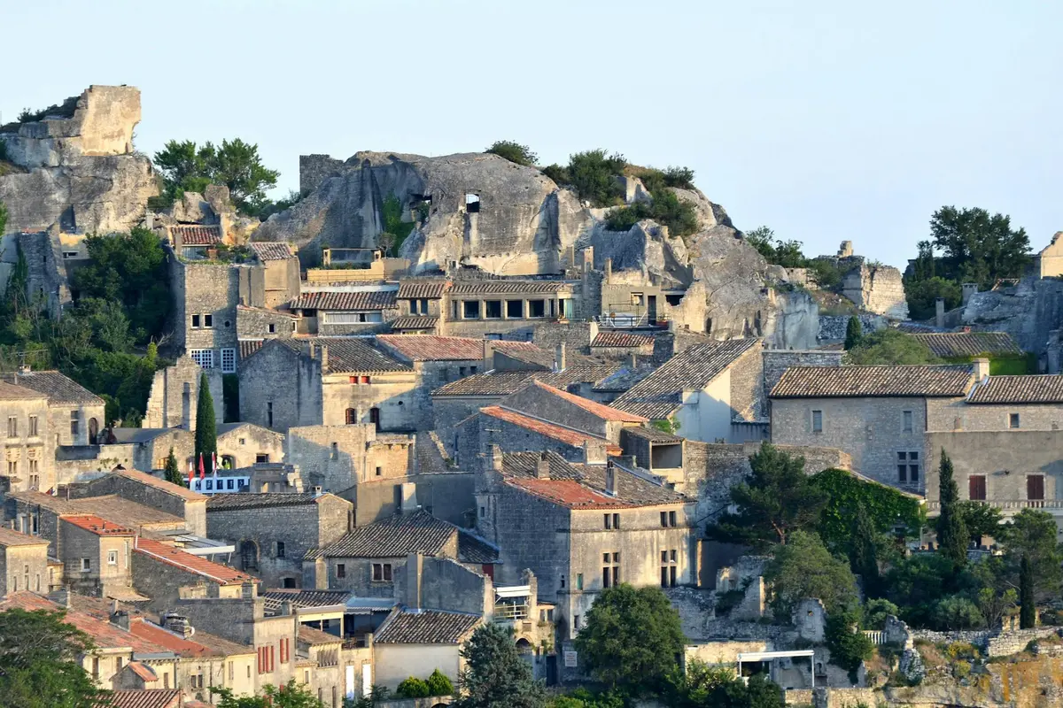 Bâtiments médiévaux en pierre regroupés sur une colline avec des falaises rocheuses et de la verdure en arrière-plan.