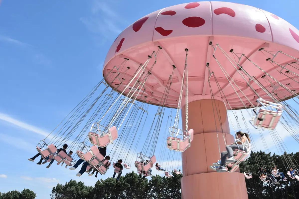Des personnes montent un carrousel rose sur fond de ciel bleu, avec des arbres en arrière-plan.