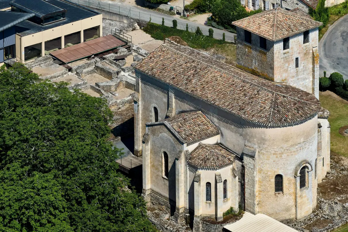 Vue aérienne d'une vieille église en pierre avec un toit en tuiles, des ruines adjacentes, des bâtiments et de la verdure à proximité.