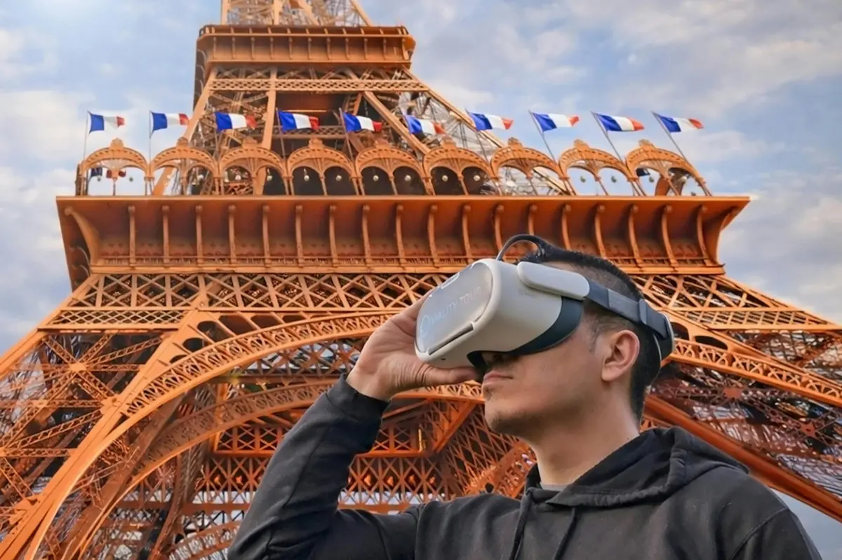 Une personne portant un casque de réalité virtuelle se tient près de la Tour Eiffel, décorée de drapeaux, sous un ciel partiellement nuageux.