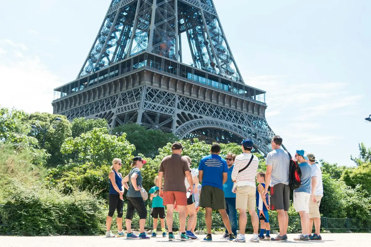 Un groupe de personnes se tenant près d'un espace vert, avec la Tour Eiffel visible en arrière-plan, par une journée ensoleillée.